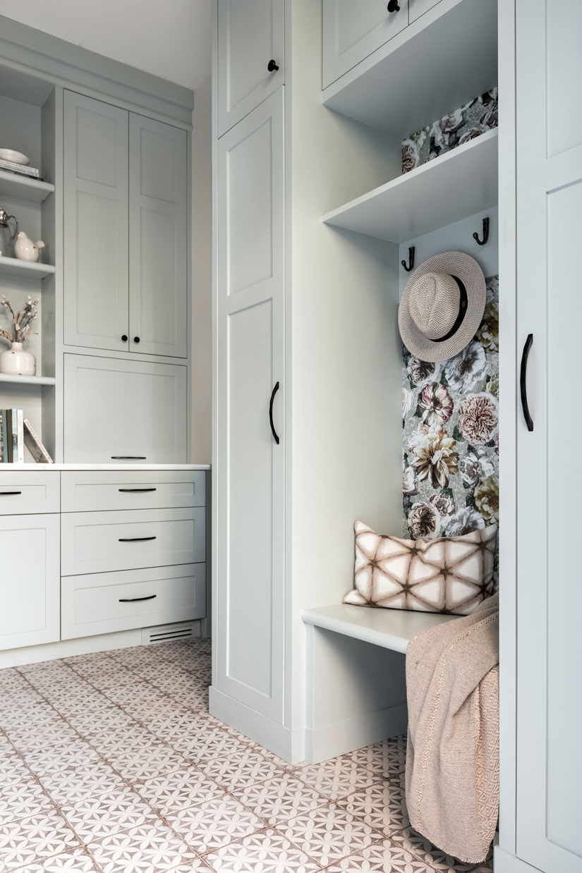 A stylish laundry room featuring floral wallpaper, a locker bench seat, modern appliances, and encaustic patterned tile flooring undergoes a renovation by a prominent Calgary interior designer.