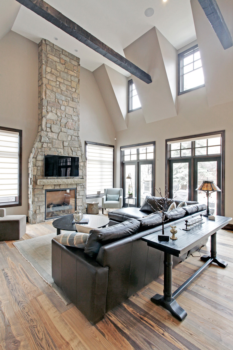Elegant stone fireplace with dark wood beams designed by a renowned New Home Designer in Calgary.