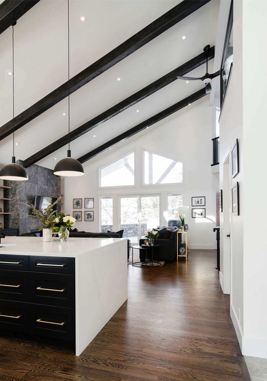 Modern kitchen with black accents, pendant lighting, and a view into an adjacent living area, designed by a top Calgary interior designer.