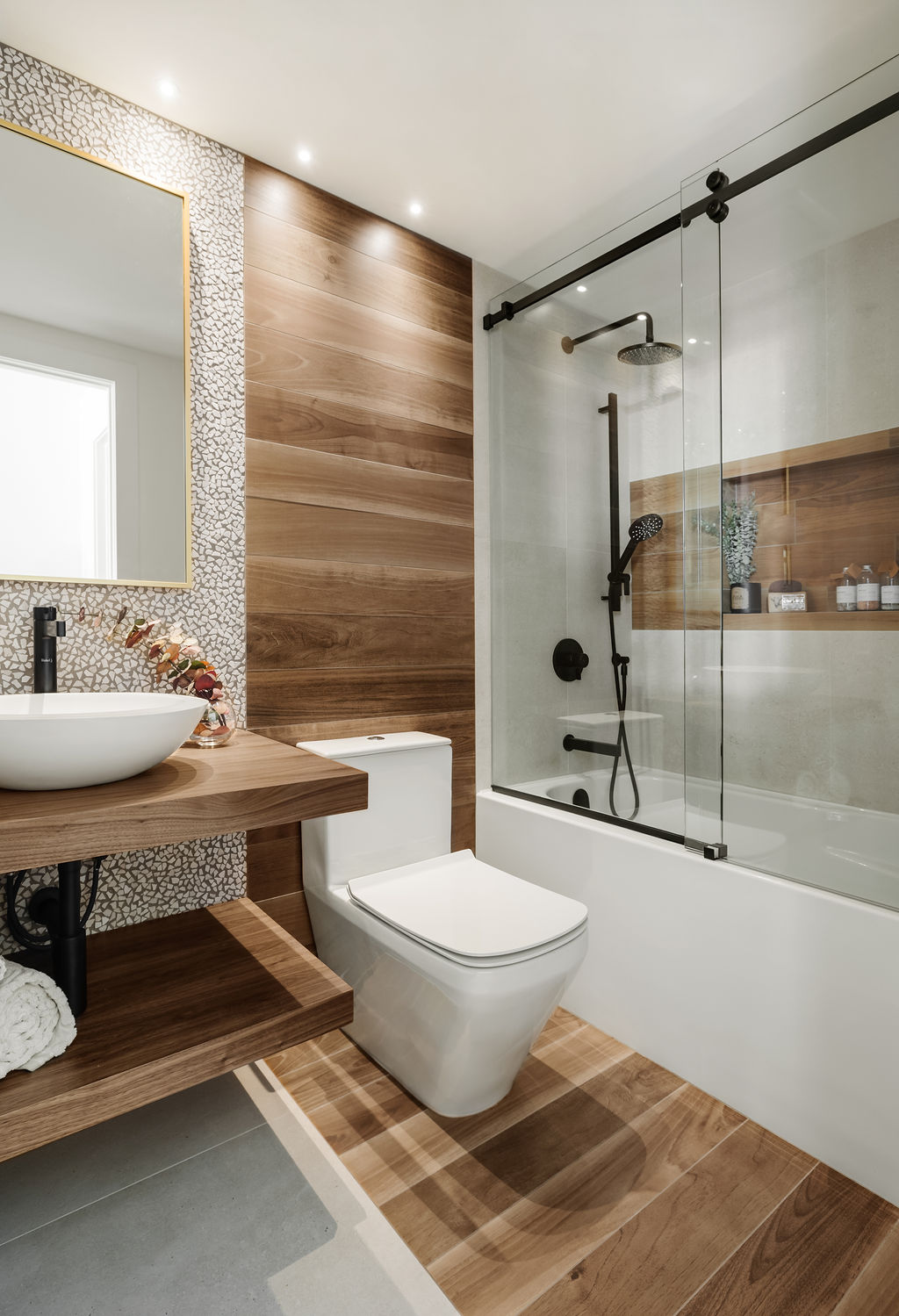 Modern bathroom with wooden accents, a vessel sink on a wooden countertop, a white toilet, and a bathtub with a glass shower enclosure.