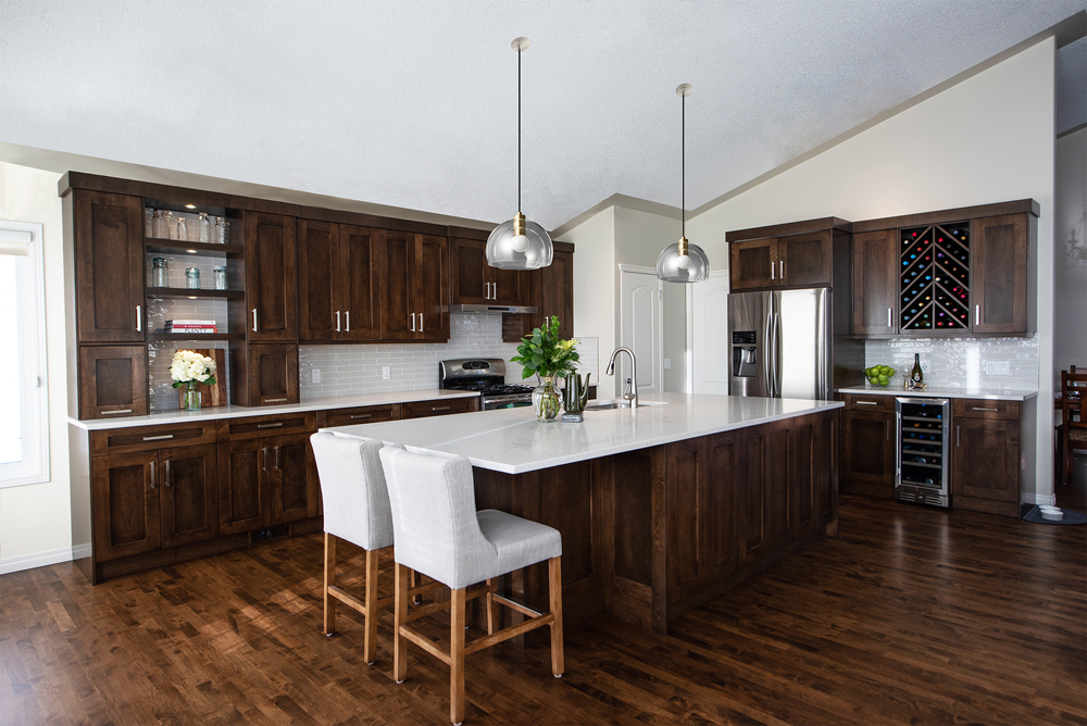 A modern kitchen with dark wood cabinets, a large island with white countertops, two upholstered stools, stainless steel appliances, pendant lighting, and hardwood floors.
