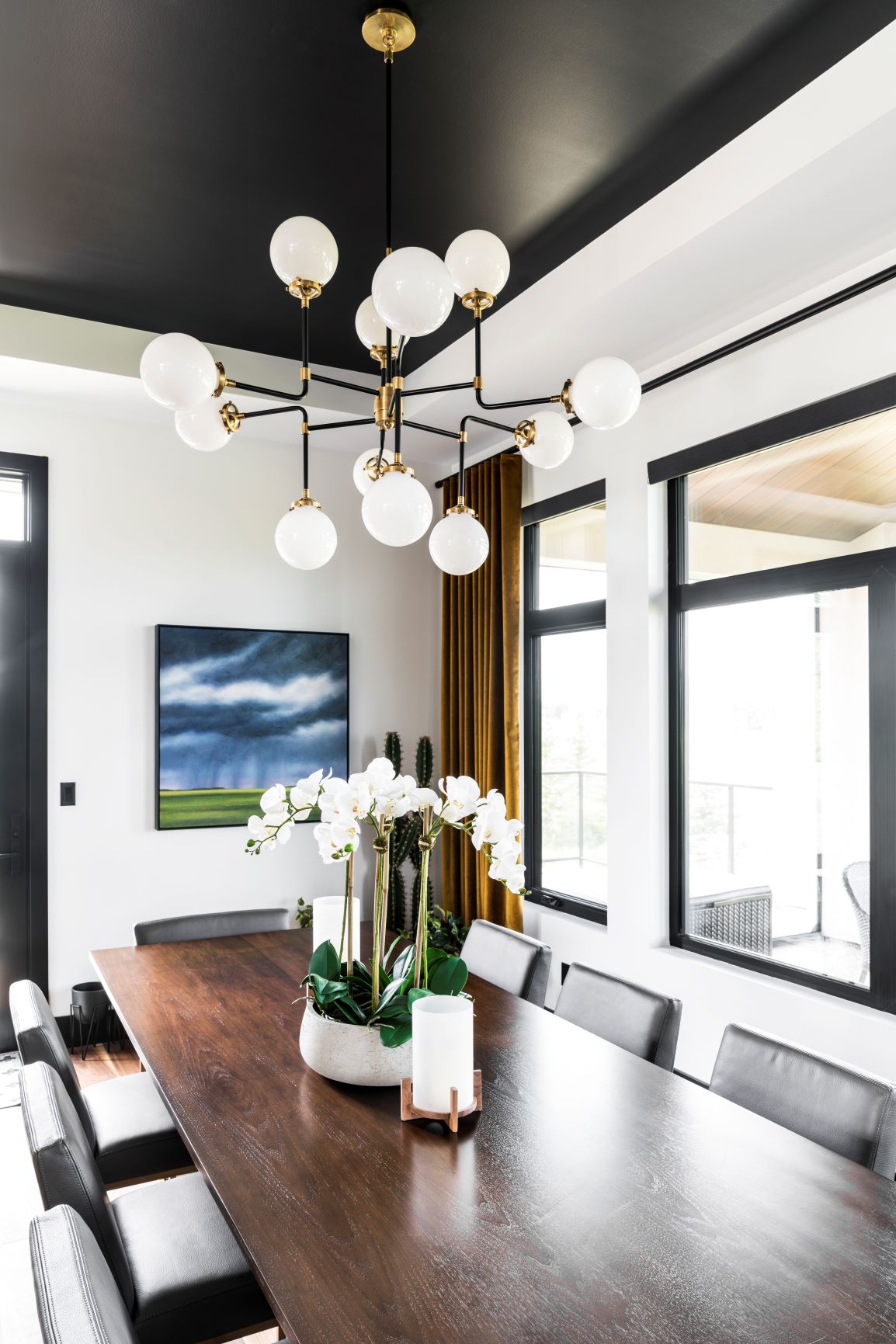 Modern dining room featuring a wooden table, black chairs, a large plant centerpiece, a unique chandelier.