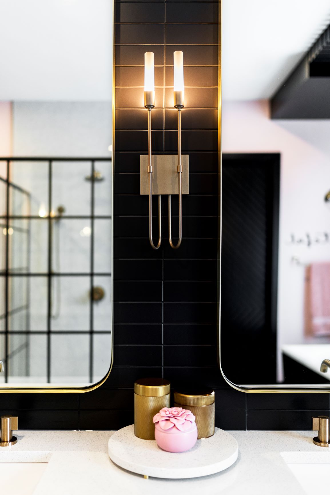 A modern bathroom features a black and white bathtub, pink wall with a "grateful" sign, hanging metallic spherical lights, and a pink towel on a gold towel rack.