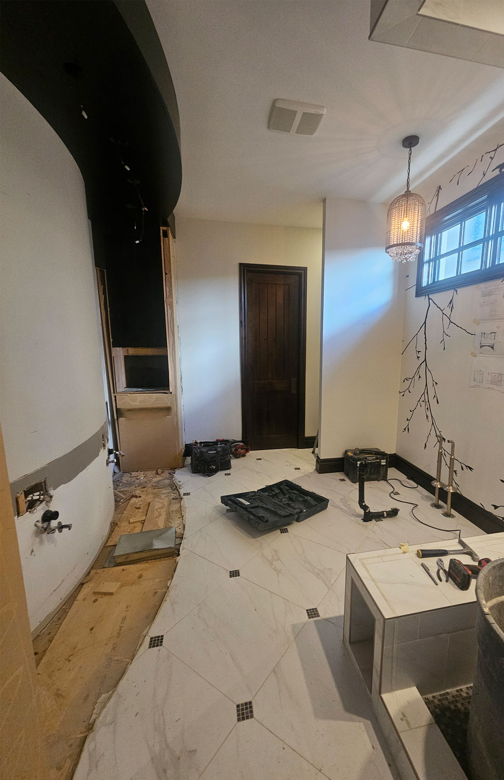 Before renovation: partially demolished industrial-style ensuite with curved dark ceiling detail, white tile flooring, dark wood trim and the original shower and tub area being removed.