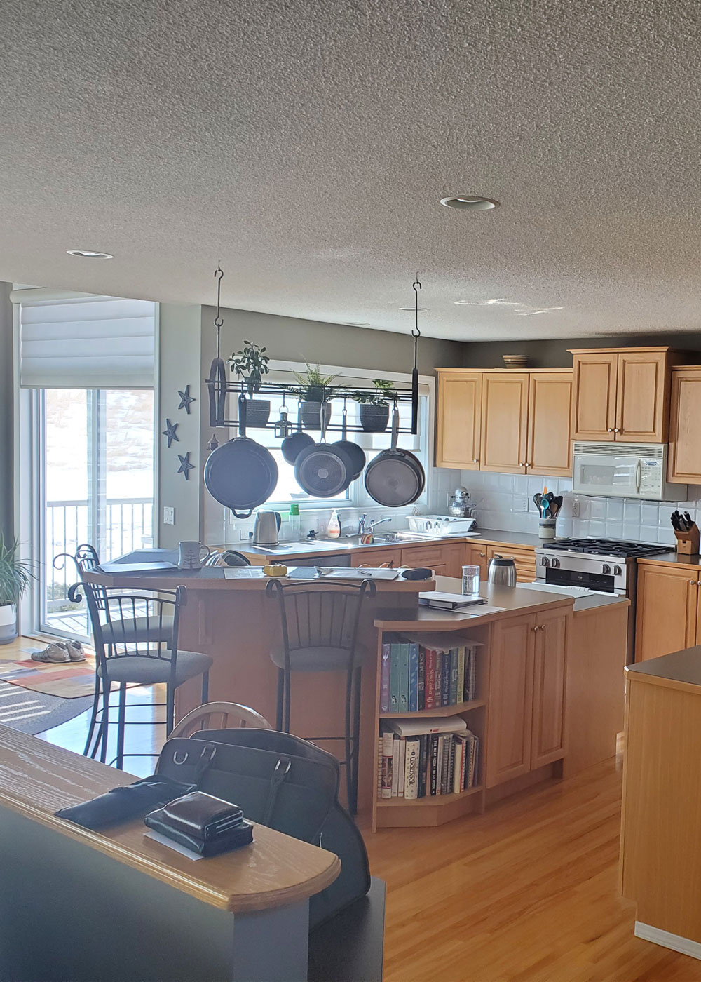 “Before renovation: dated Calgary kitchen with oak cabinetry, laminate countertops, peninsula seating and hanging pot rack.”