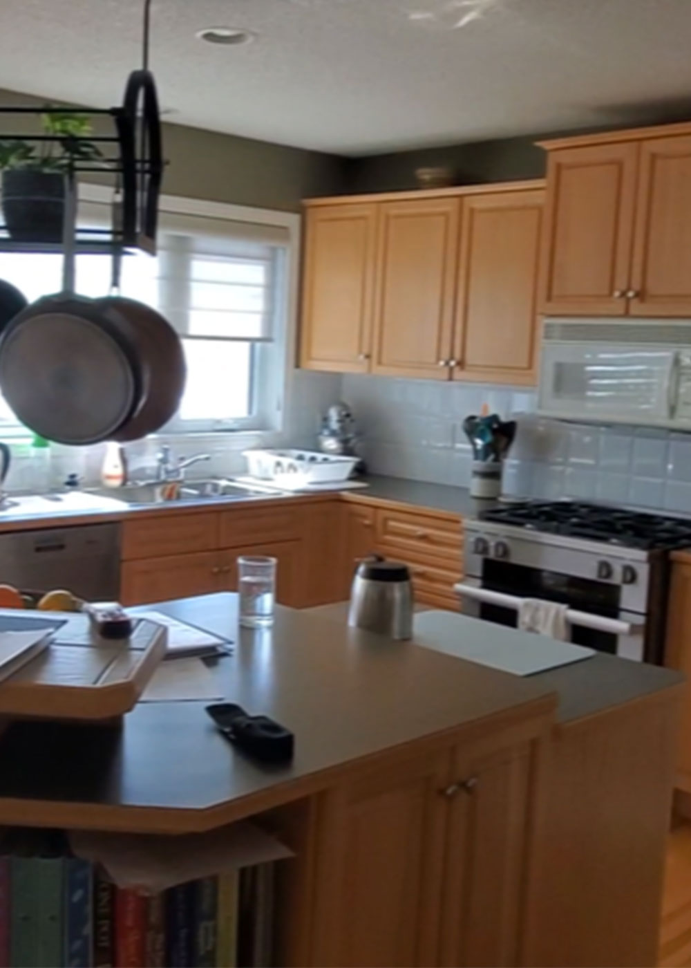 “Before renovation: dated Calgary kitchen with oak cabinetry, laminate countertops, peninsula seating and hanging pot rack.”