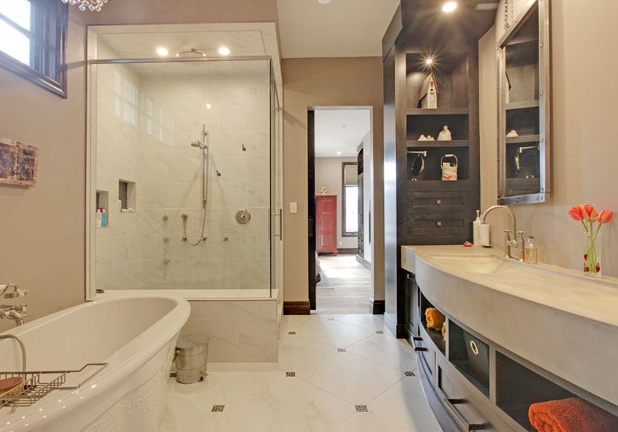 Before renovation: industrial-style ensuite with dark custom cabinetry, concrete-look double vanity, glass-enclosed shower, freestanding tub and warm brown walls.